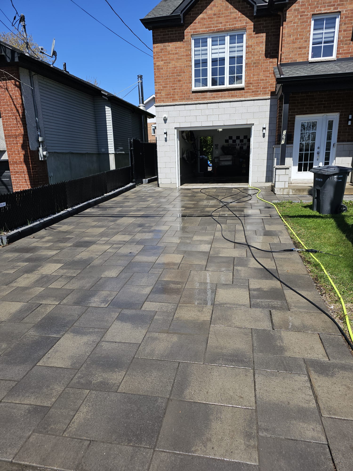Freshly pressure washed interlocking paver driveway in front of brick two-story home