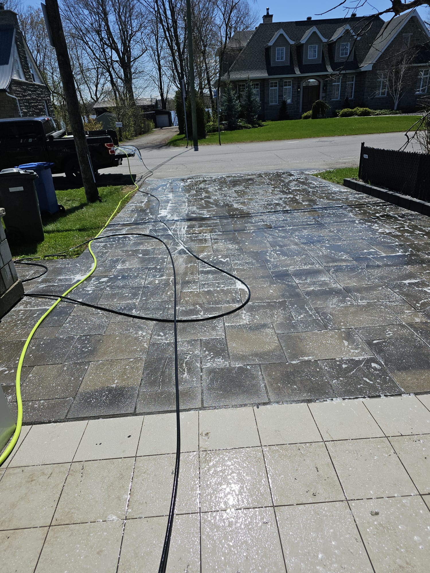 Large interlocking stone driveway mid-clean with pressure washer, residential street