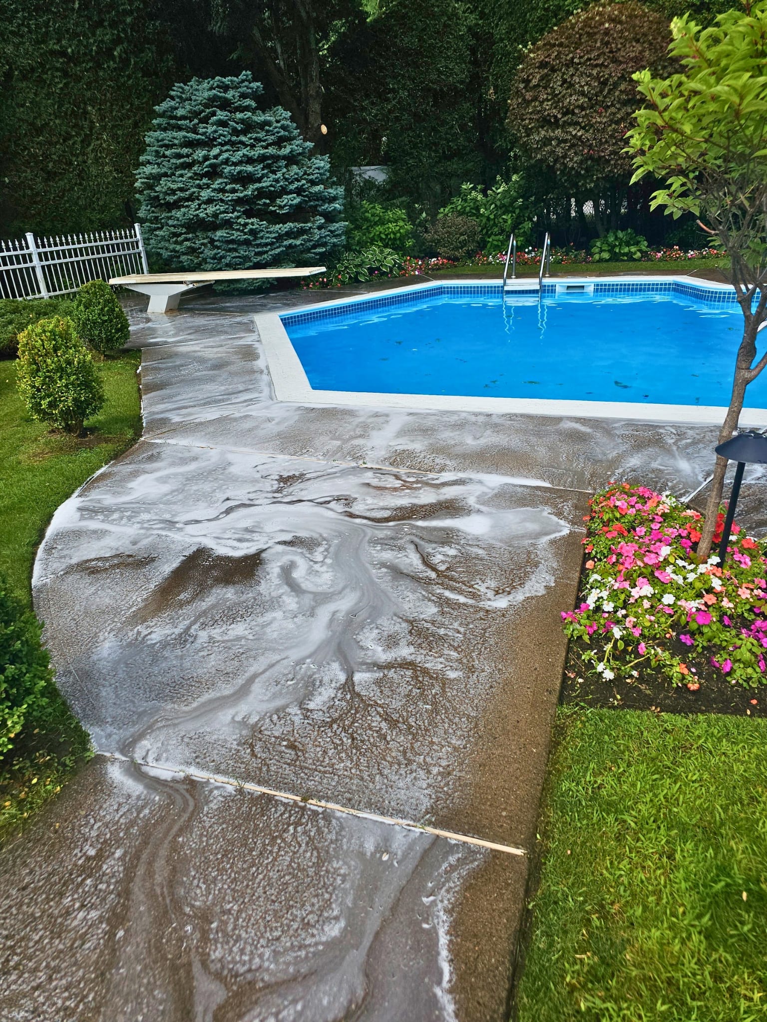 Concrete pool surround being pressure washed next to blue inground pool